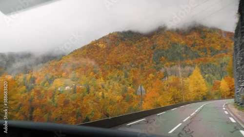 A camping van driving on a mountain road in the French Alps during autumn, col des gets, with golden trees and fallen leaves. Pan to left. photo