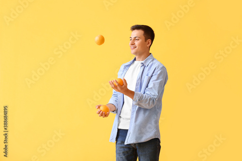 Handsome man juggling ripe oranges on color background photo