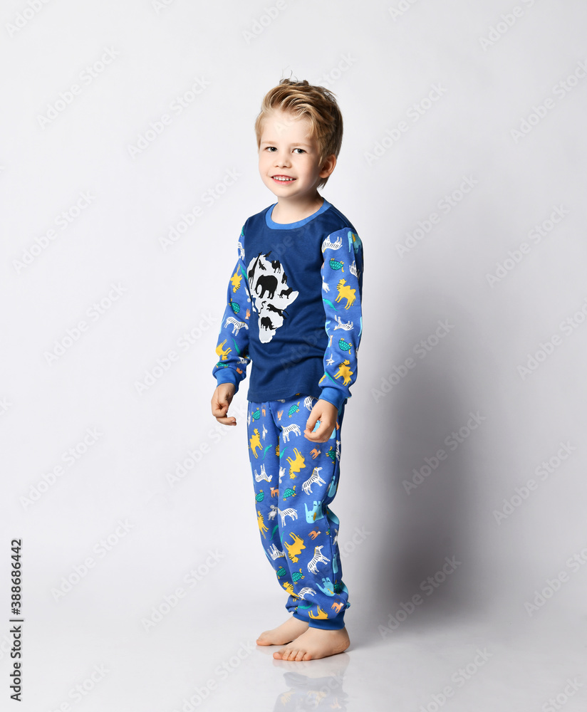 Nice blond kid boy in pyjamas with african animals pattern and map print is getting ready for bed, going. Side view Nice blond kid boy in pyjamas with african animals pattern and map print is getting ready for bed, going. Side view