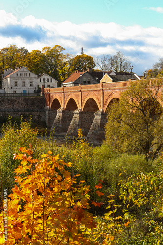 Sunny view with old brick bridge over river Venta. Photo taken on a warm autumn day, yellow leaves.
