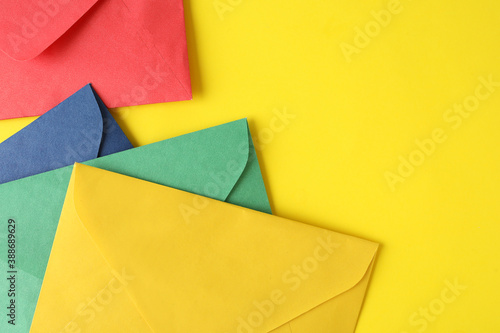 Colorful paper envelopes on yellow background, top view. Space for text