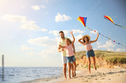 Happy parents and their child playing with kites on beach near sea. Spending time in nature