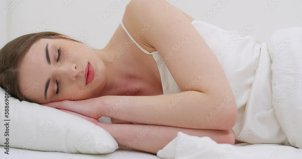 Young female sleeping in bed, waking up in the morning, close-up of a female face, woman opens her eyes and looks into the camera. Young female sleeping in bed, waking up in the morning, close-up of a female face, woman opens her eyes and looks into the camera.