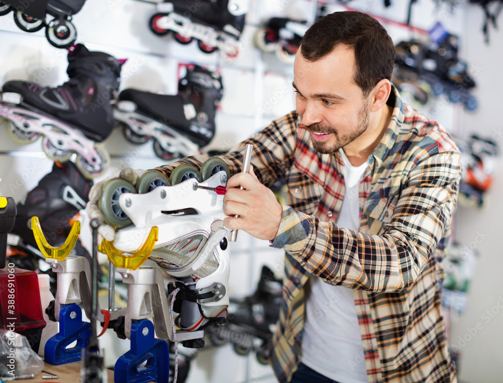 Satisfied smiling male master fixing roller-skates in sports store