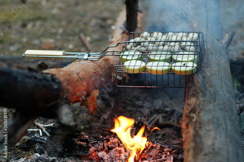 Vegetables are grilled in the forest. Delicious zucchini and mushrooms on the grill. Vegetarian dish on a campfire in the wild. Delicious zucchini and mushrooms on the grill.