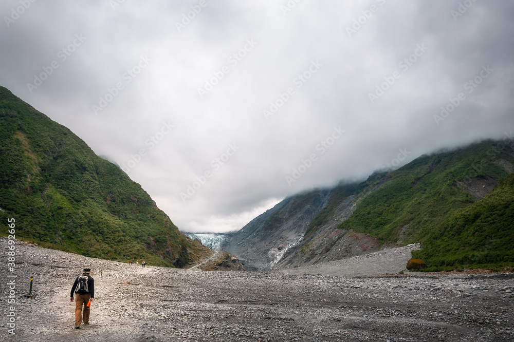 Active traveler hiking on the trail to the Franz Josef Glacier in the distance in the Southern Alps of New Zealand, one of the iconic destinations in the Southern Island.