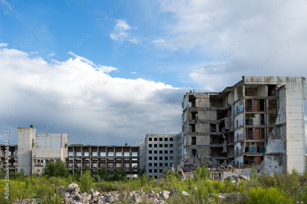 The remains of a large destroyed building against a blue sky with clouds with gray concrete debris in the foreground.