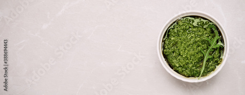 Bowl of tasty arugula pesto and space for text on light table, top view. Banner design