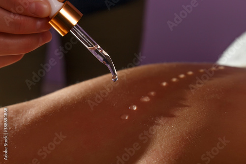 Hand of a masseur applying oil drops on a female back