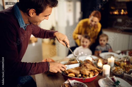 Fotografía Happy man carving meat during Thanksgiving dinner at dining table