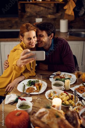 Happy couple taking selfie while having Thanksgiving dinner at dining table.