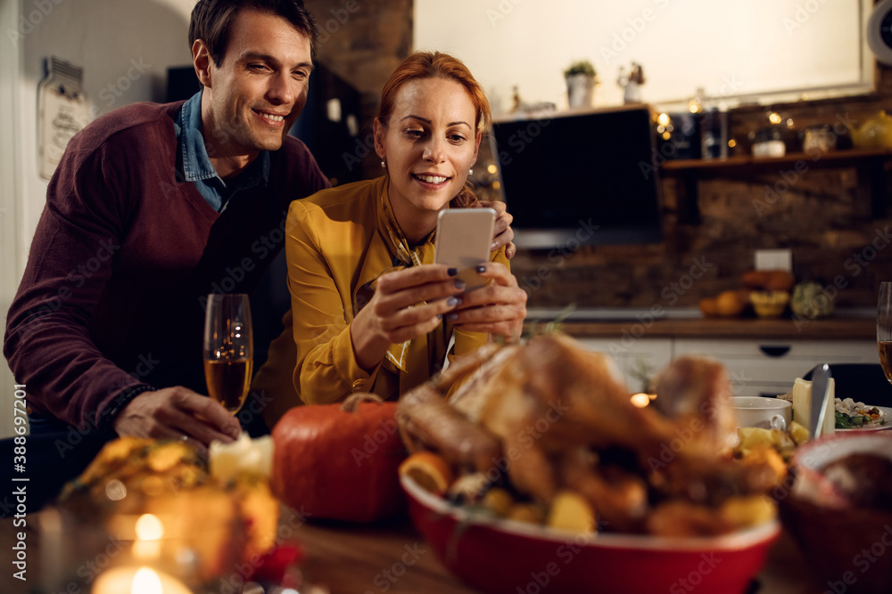 Happy couple taking picture of their Thanksgiving turkey at dining table.
