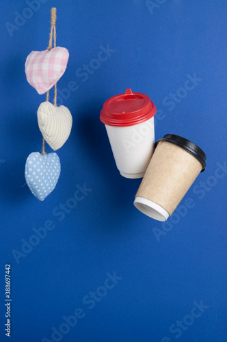 disposable paper flying coffee cups with textile hearts on a blue background hanging on. Takeaway coffee concept. I love coffee photo