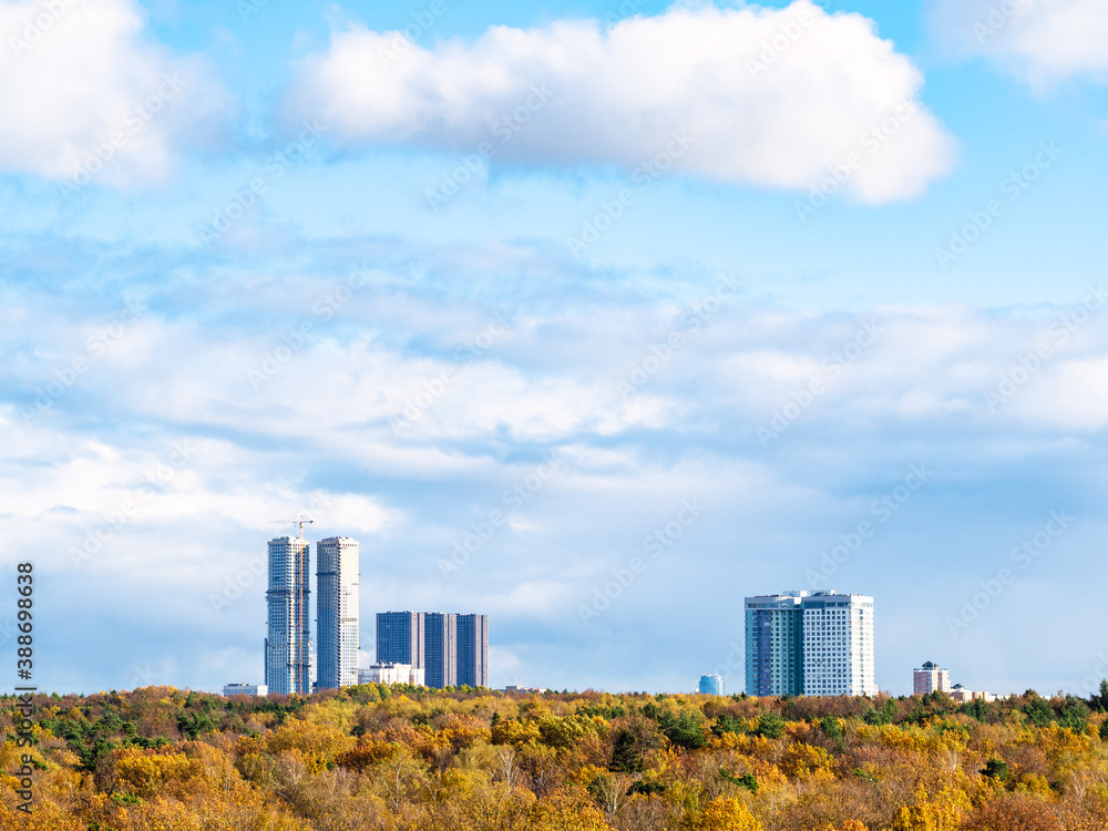 blue sky with white clouds over yellow forest and high-rise houses on horizon on sunny autumn day blue sky with white clouds over yellow forest and high-rise houses on horizon on sunny autumn day