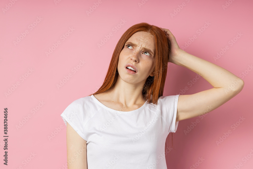 Pensive young caucasian ginger female with freckled skin long hair wearing white t shirt looking up with puzzled expression, touching lips with forefinger, thinking isolated blue background.Copy space Pensive young caucasian ginger female with freckled skin long hair wearing white t shirt looking up with puzzled expression, touching lips with forefinger, thinking isolated blue background.Copy space