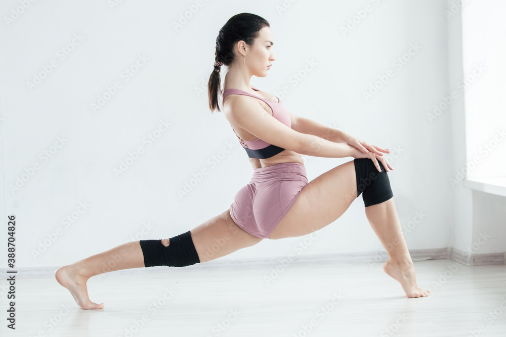 Attractive young woman does a stretching exercise on the floor looking at camera