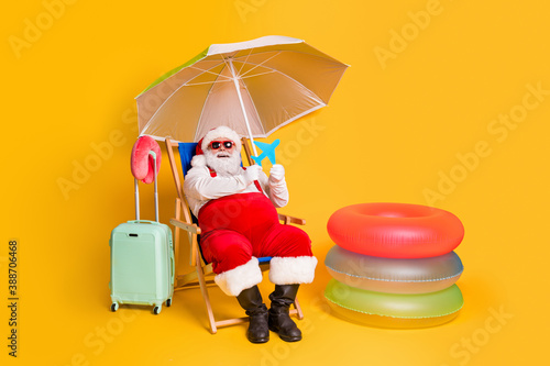 Full size photo of grey white hair bearded santa claus relax chill chaise-lounge x-mas christmas hold paper card plane wear red sunglass cap hat isolated yellow color background
