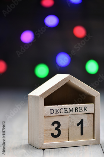 Christmas decorations on a wooden background: wooden cubes with the numbers December 31, and blurry garland in the background. Vertical photo