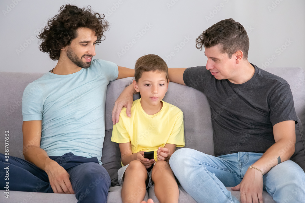 Positive gay dads and son watching TV show together at home, sitting on  couch in living room, smiling and hugging boy. Family and home  entertainment concept Photos | Adobe Stock