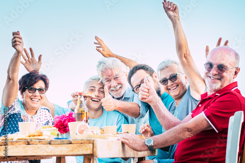 Group of people family have fun and enjoy celebration outdoor - caucasian men and women laugh around a wooden table with food and drinks - birthday with old and young
