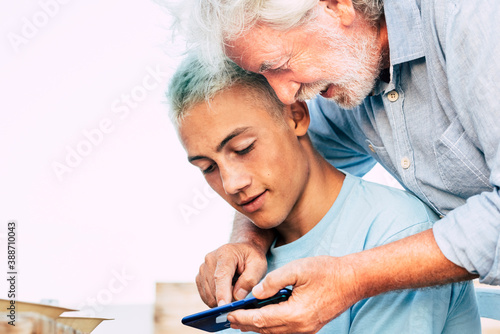 Portrait of young and old people grandfather and grandson together using a modern smart phone - family and friends concept with teenager and senior man enjoying technoogy together photo