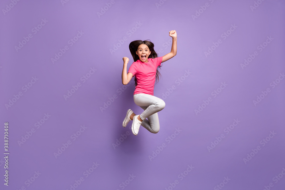 Full length body size photo of jumping high cute little girl celebrating win cheering shouting smiling isolated on purple color background