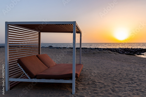 Empty double sun bed on the sandy beach in Dubai  with orange sunset in the background and calm sea.