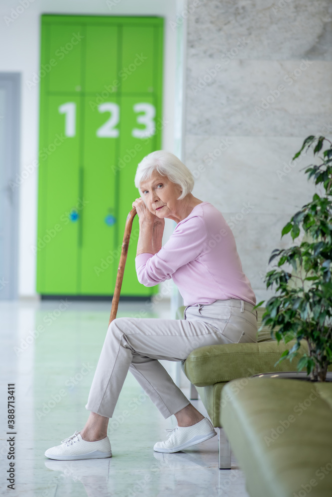 © zinkevych - Grey-haired woman with a walking stick sitting in the corridor
