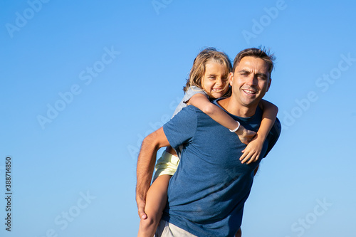 Happy dad carrying cheerful girl on his back. Father and daughter enjoying leisure time together outdoors. Family and walking outdoors concept
