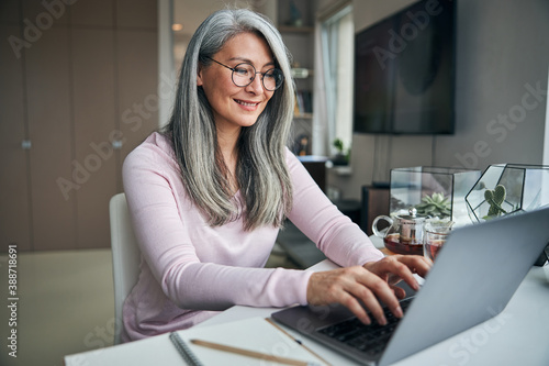 Cheerful woman in glasses working on laptop at home photo
