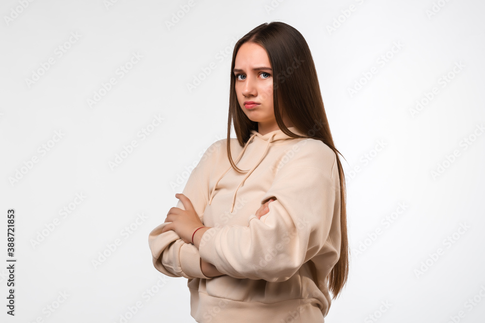 Photo of Offended girl holding hands crossed, looking at camera. Studio shot, white background. Human emotions concept Photo of Offended girl holding hands crossed, looking at camera. Studio shot, white background. Human emotions concept
