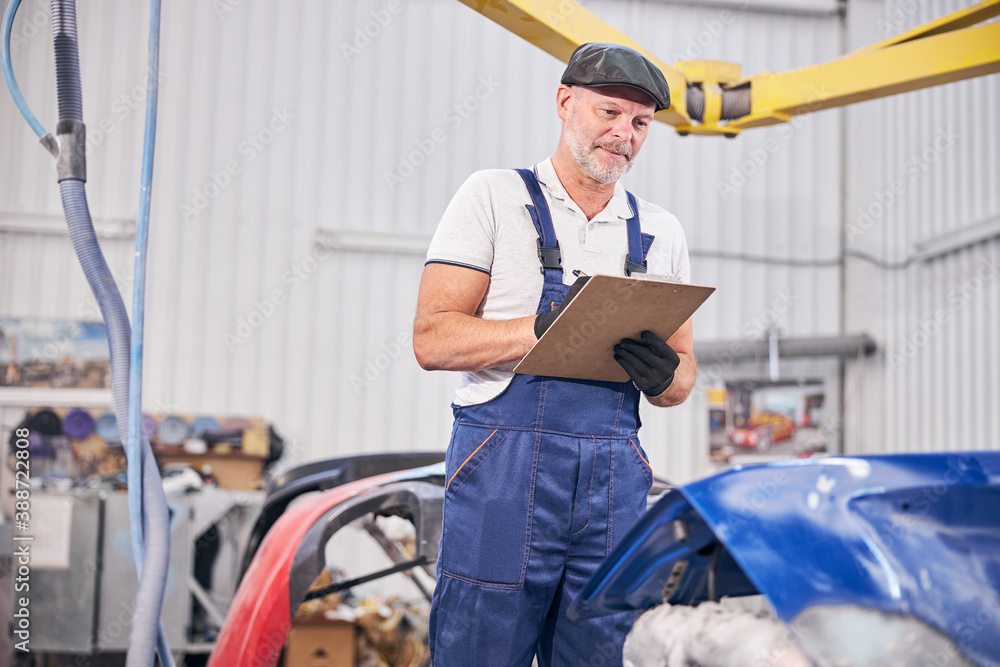 Handsome auto mechanic writing on clipboard at car repair shop Handsome auto mechanic writing on clipboard at car repair shop