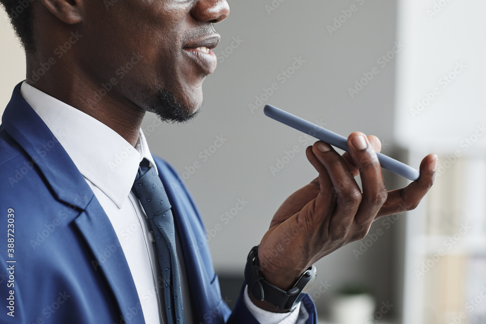 Close-up of African man in suit holding mobile phone and talking on it or recording an audio message Close-up of African man in suit holding mobile phone and talking on it or recording an audio message