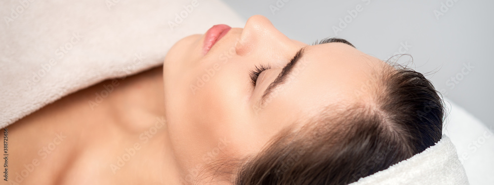 Side view of young woman lying on beautician table with closed eyes while waiting for cosmetic procedure in beauty salon
