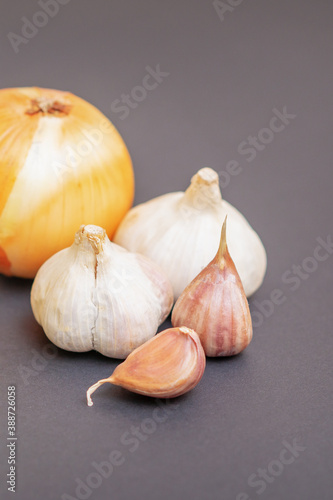 Unpeeled raw bulb and clove of garlic and onion on black surface with empty space for text