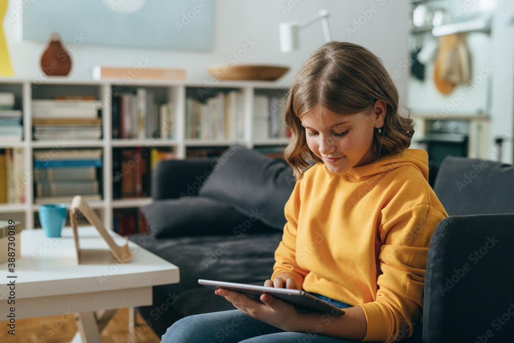 teenage girl using tablet computer while sitting on sofa in living room