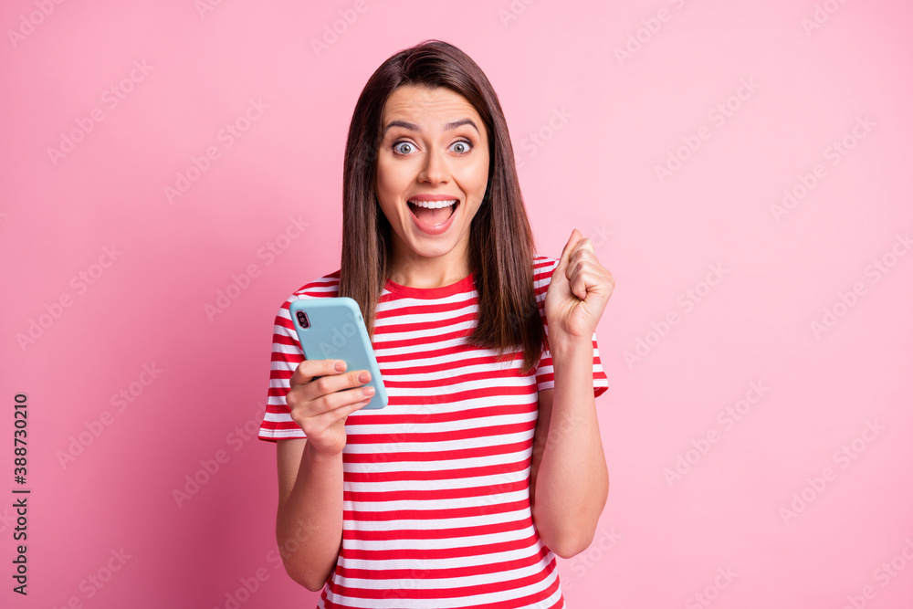 Photo portrait of girl wearing striped t-shirt keeping smartphone gesturing like winner isolated on pastel pink color background Photo portrait of girl wearing striped t-shirt keeping smartphone gesturing like winner isolated on pastel pink color background