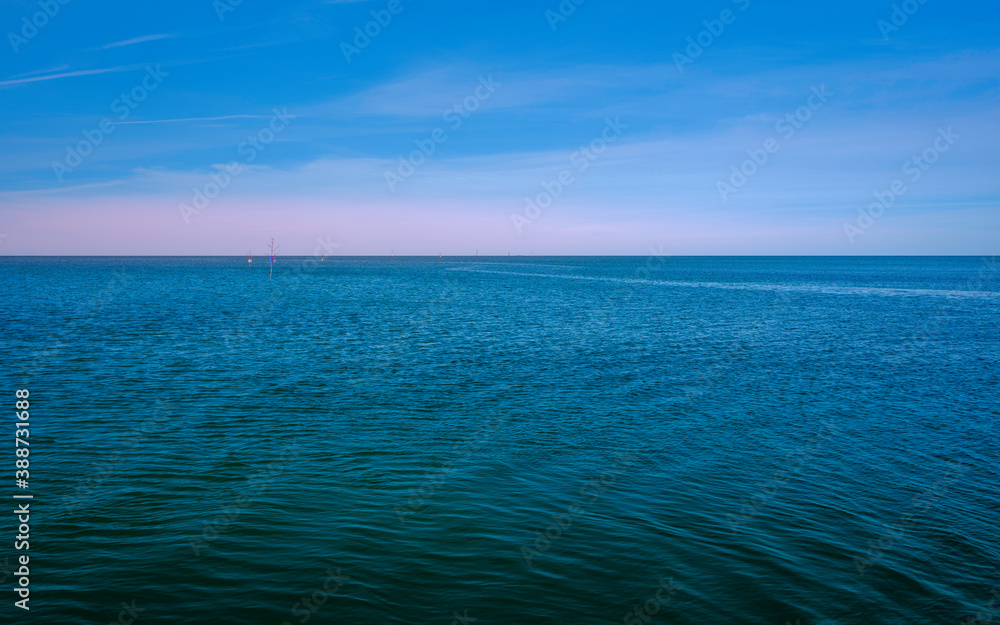 Tranquil seascape with gentle blue waves and soft white clouds on the blue sky background at dusk