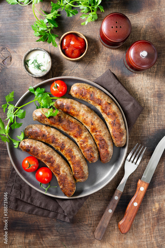Fried sausages. Grilled sausages with spices, sauce, tomatoes and parsley. Delicious meat sausages in a ceramic plate
