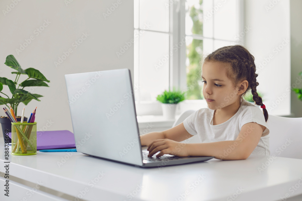 Online education. Video lesson school for children. A little girl is watching a video lesson in a laptop sitting at a table in the room.