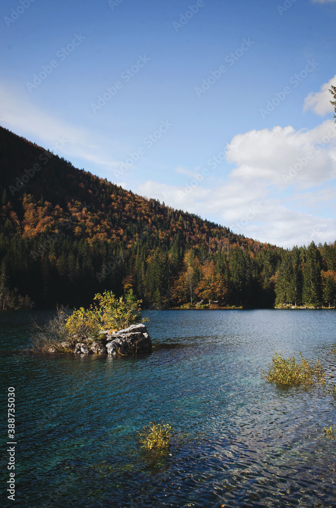 Scenic view on the blue italian lake against the colorful autumn forest in mountains.