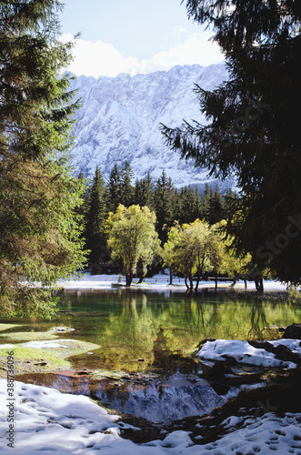 Autumn landscape of mountains covered in snow and reflected in blue italian lake.