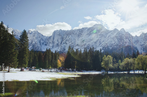 Autumn landscape of mountains covered in snow and reflected in blue italian lake.