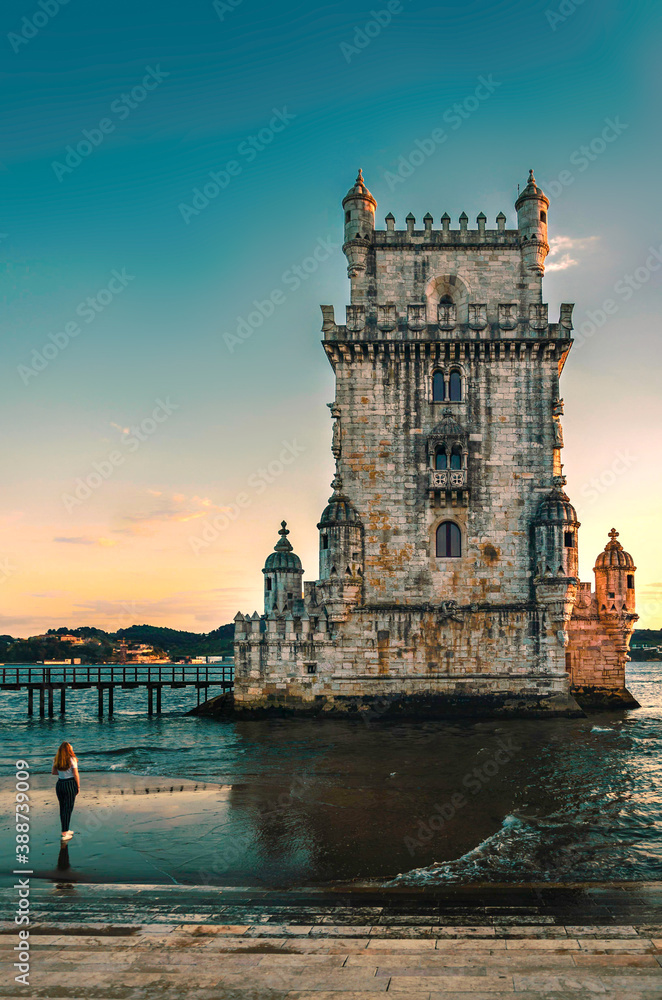 Lisbon, Portugal, Belem Tower (Torre de Belém) on the Tagus River - 03/23/2019. Woman looking at the tower at sunset in summer.