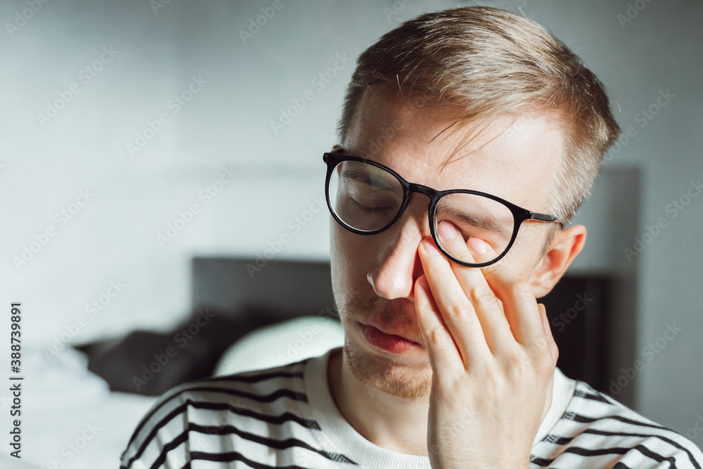 Young man in eyeglasses feeling exhausted, looking tired after reading, Frustrated millennial rubbing eyes in home office. Sight loss, blurry vision,  optician syndrome, pressure relief, stress work