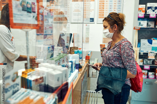 Woman shopping at pharmacy, buying medicines, wearing face mask to cover mouth and nose during pandemic coronavirus outbreak
