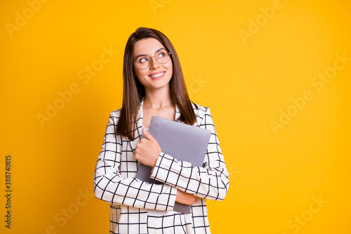 Photo portrait of dreamy girl keeping hugging computer looking at empty space smiling isolated on bright yellow color background