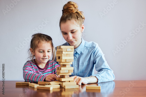 Little girl preschooler and her elder sister playing together with wooden blocks game toy. Siblings spending time sitting at desk at home