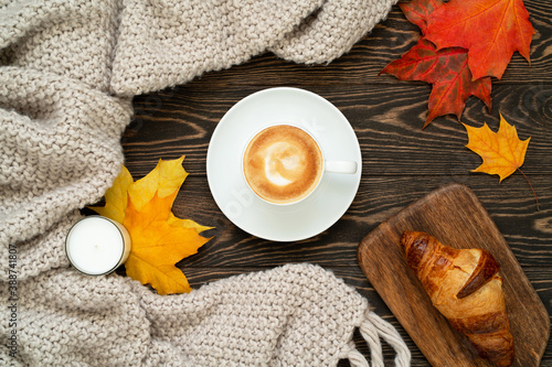 Top view of a cup of coffee  fresh croissant  candle  colorful maple leaves and knitted plaid on the wooden table. Autumn flat lay. Morning ritual.