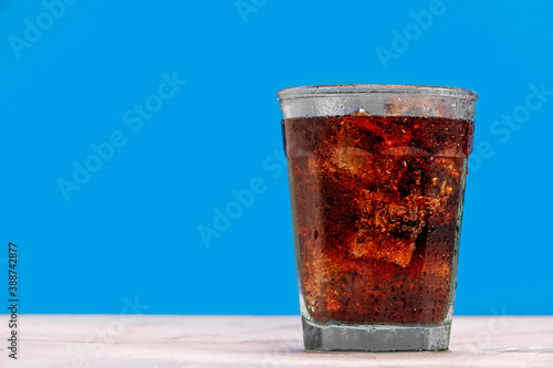 Принти на полотні Ice cold glass of soda, cola, fizzy drink, carbonated beverage sits against a blue wall with ice cubes and condensation on the glass making it refreshing and inviting